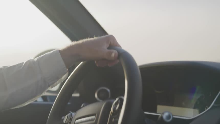 A driver turns a steering wheel with one hand as the car shakes while moving