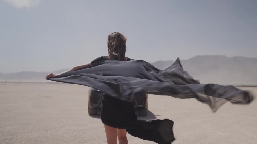 A woman on the middle of desert with a fluttered cape on her back