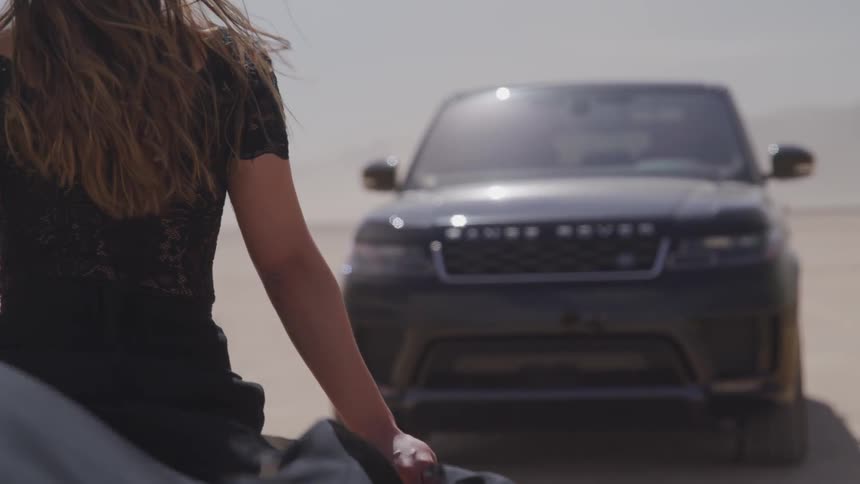 Woman walks towards a vehicle while holding billowing fabric behind her