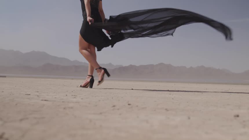 Model walking across desert road in heels with dress flowing behind her
