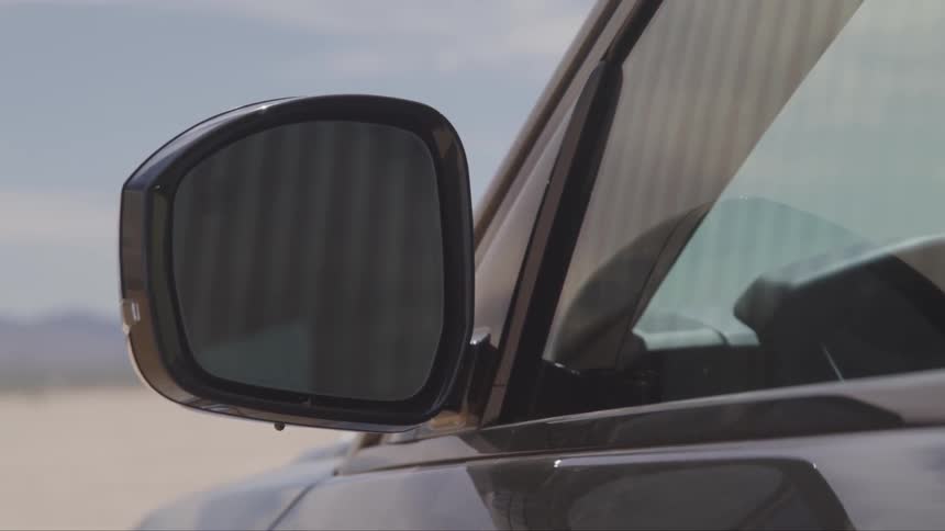 A mirror is on the side of a car parked in a desert