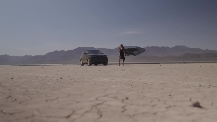 A woman stands next to the car in the desert