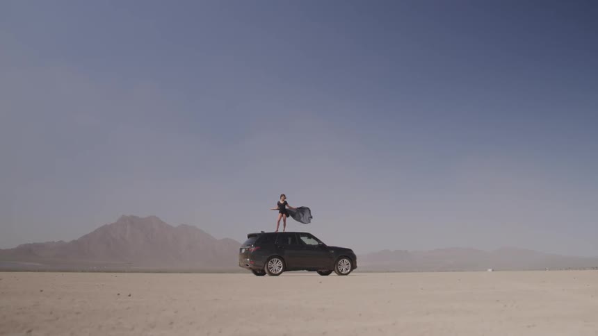 Woman stands on top of car in the middle of windy desert