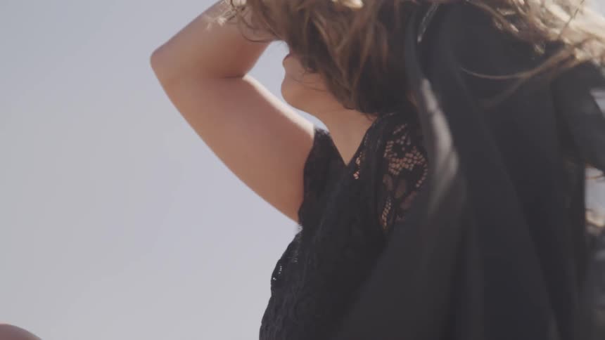 A woman is standing outdoors with wind blowing her hair