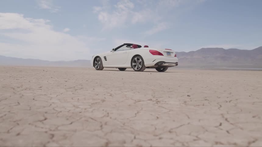 A white convertible sits on the cracked desert ground