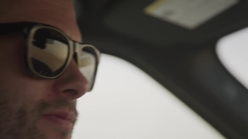 A man wearing sunglasses drives a car
