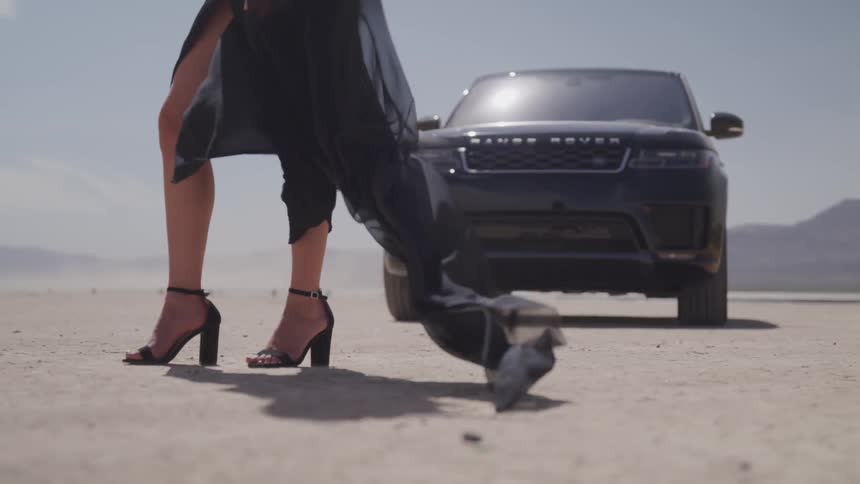A woman in heels stands in front of a black range rover parked on the salt flats