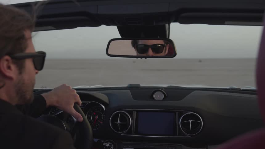 Man wearing sunglasses looks in rear view mirror while driving the car