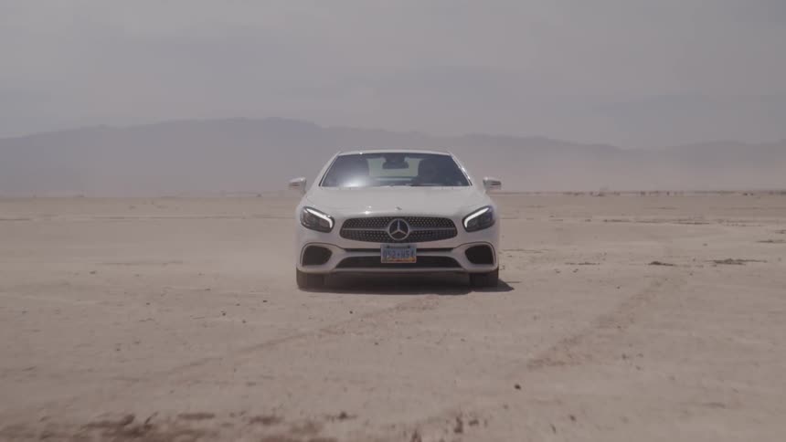 A white mercedes travels across sand in a desert