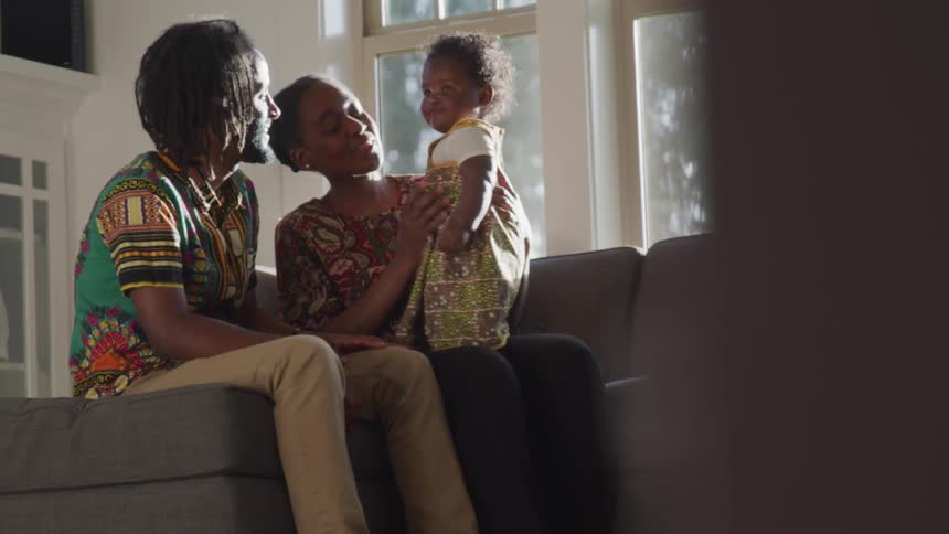 Two people play with a happy baby in a living room
