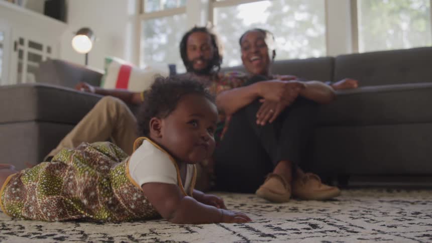 A man and a woman sitting on the floor watching a baby crawl