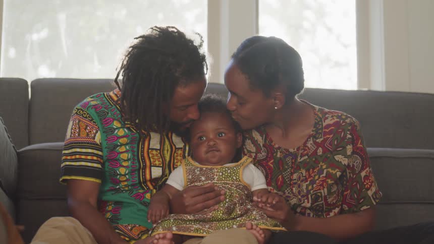 Two adults hug and kiss an adorable chubby baby
