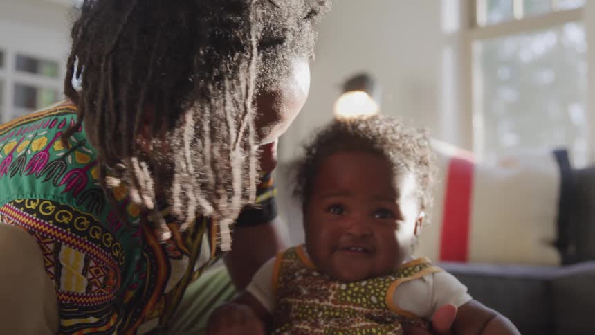 A man holds and plays with his daughter while seated in a living room