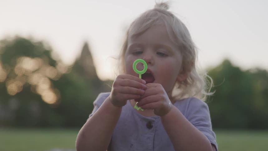 A girl holds up a wand and blows bubbles in the yard at sunset