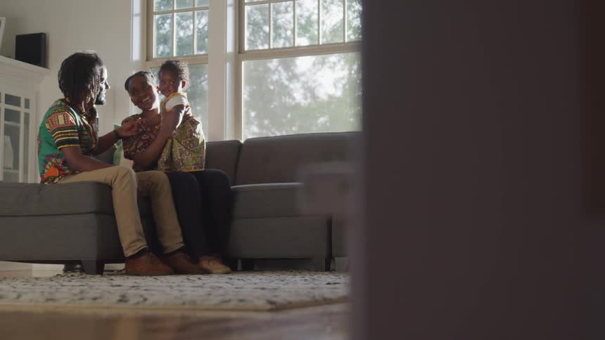 A couple holds a baby and talking together sitting on a couch
