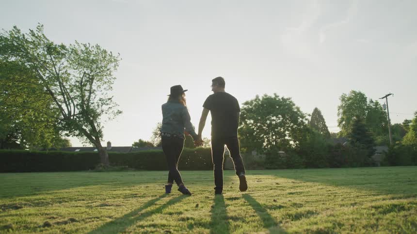 A couple walk across a lawn holding hands