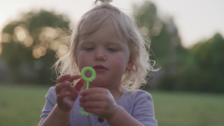 Little blonde girl blowing bubbles outdoors at the park