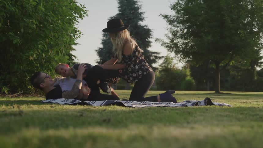 Family of four playing on a blanket on the grass at the park