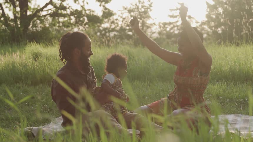 Young family playing with their baby on a blanket outdoors on the grass