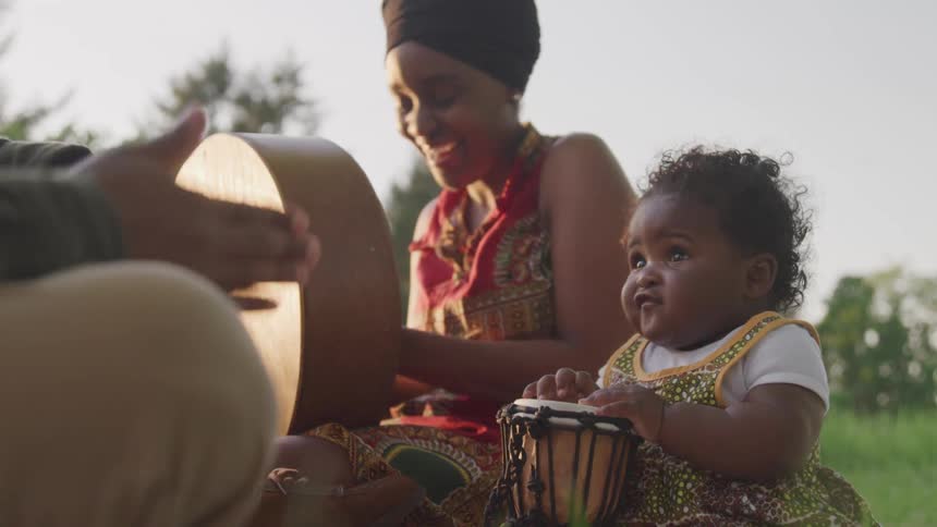 Adults sitting in a field playing drums with a baby