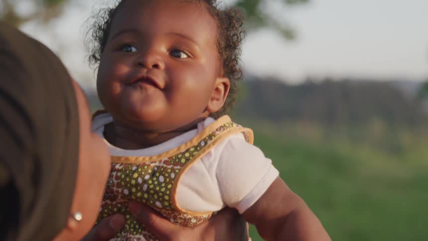 A woman is holding her daughter outside and bounces her up and down