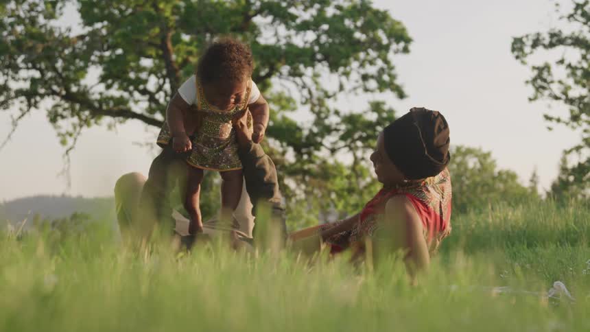 A family lies in the grass and the dad lifts his daughter up above his chest