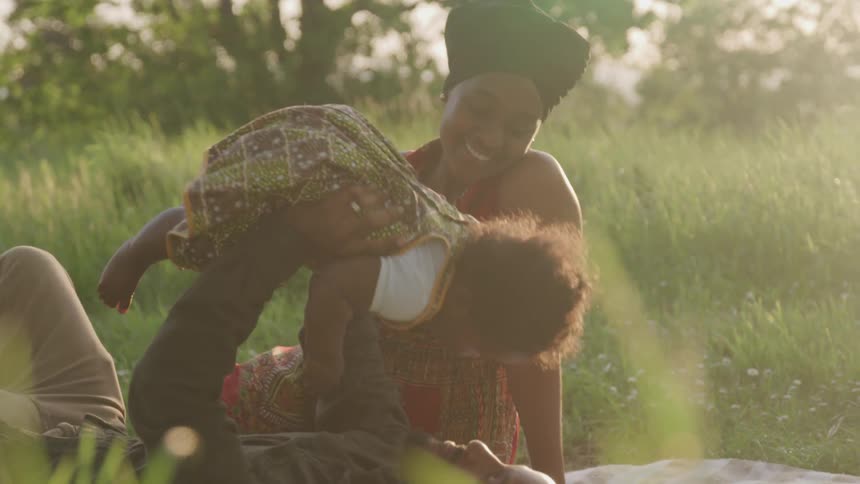 A couple play with their baby in a tall grass yard