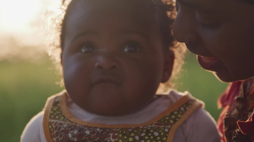 A woman bounces a baby on her lap and talks closely in her ear