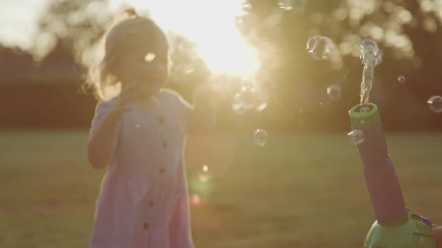 A young girl runs and jumps through bubbles in a yard
