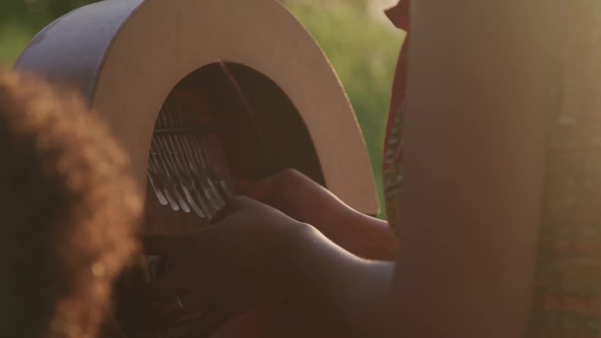 A woman sits and plays a large thumb harp while a young child is watching nearby