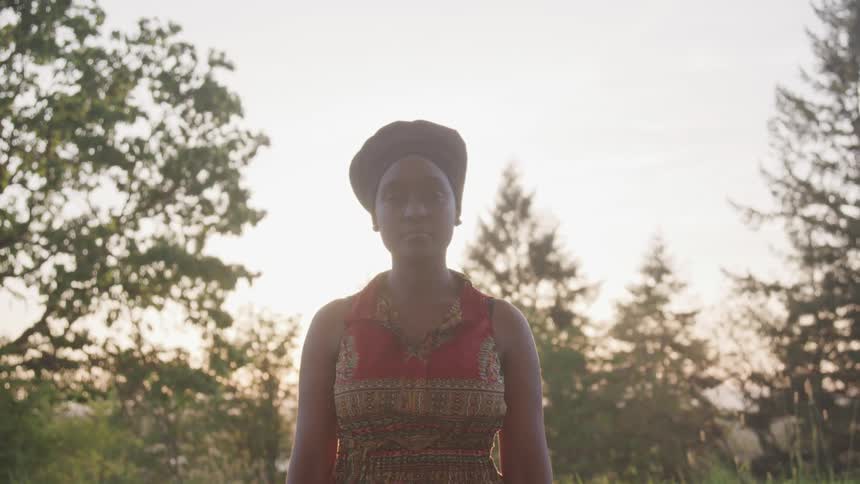 A woman stands in a grassy field with trees around