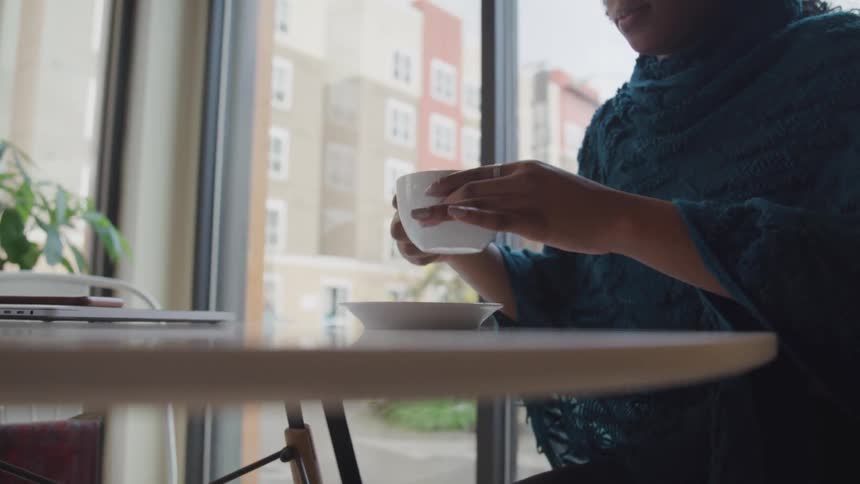 A woman is indoors and drinking coffee