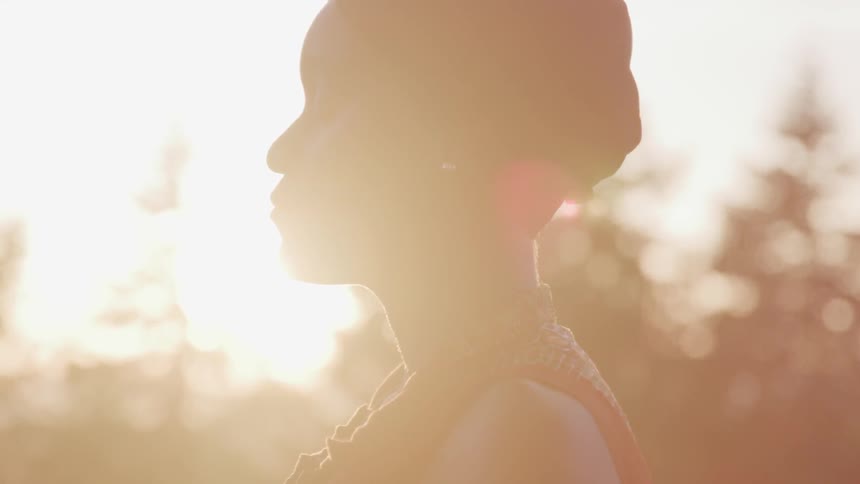 A woman standing outside with her eyes close with the sun in the background