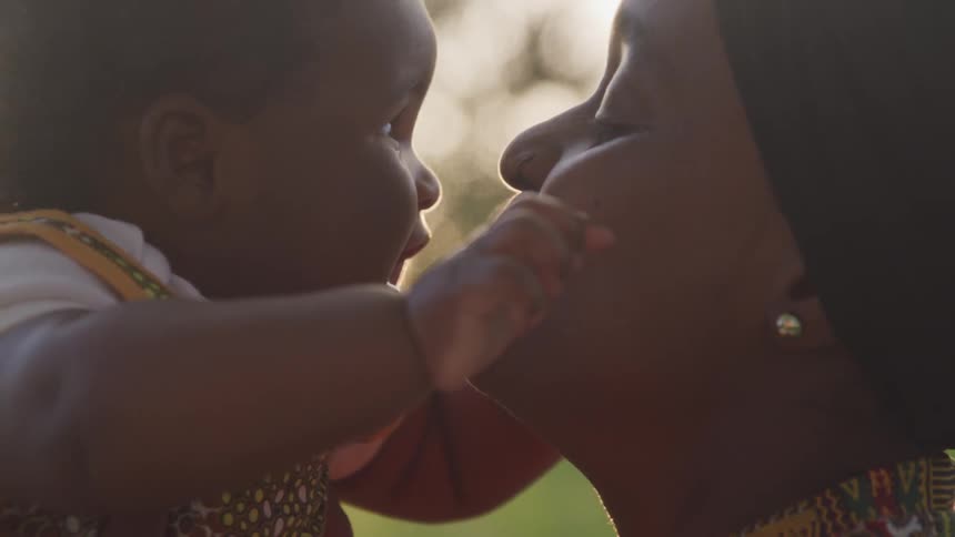 A woman holds her baby girl and kisses her on her plump cheek