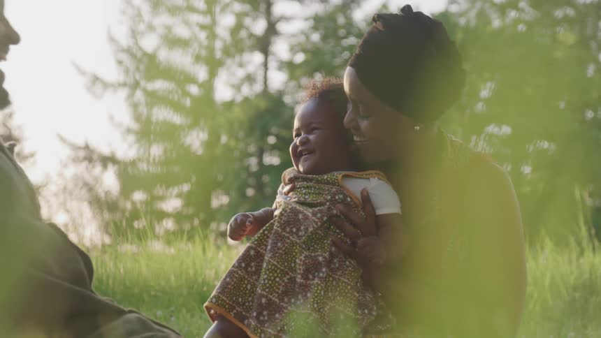 Two adults play with a laughing baby in a sunny field