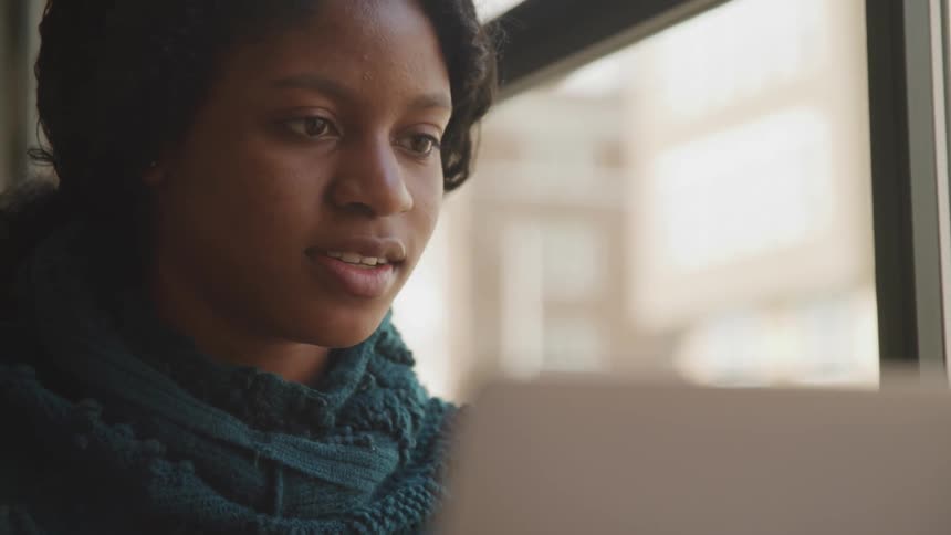 A young woman looks at her laptop screen types something and smiles