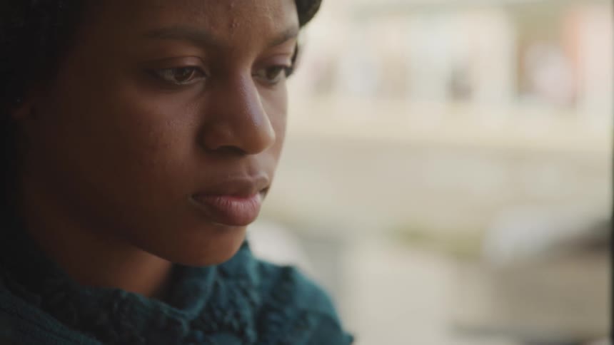 A woman stares at something off screen while pedestrian move past her on the street
