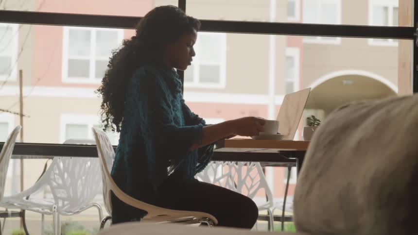 A woman sips coffee while working on her laptop in a cafe