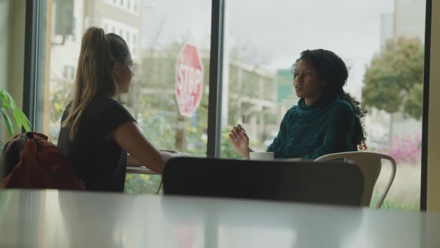 Black woman and white woman sit at the table and have a conversation in a cafe during daylight