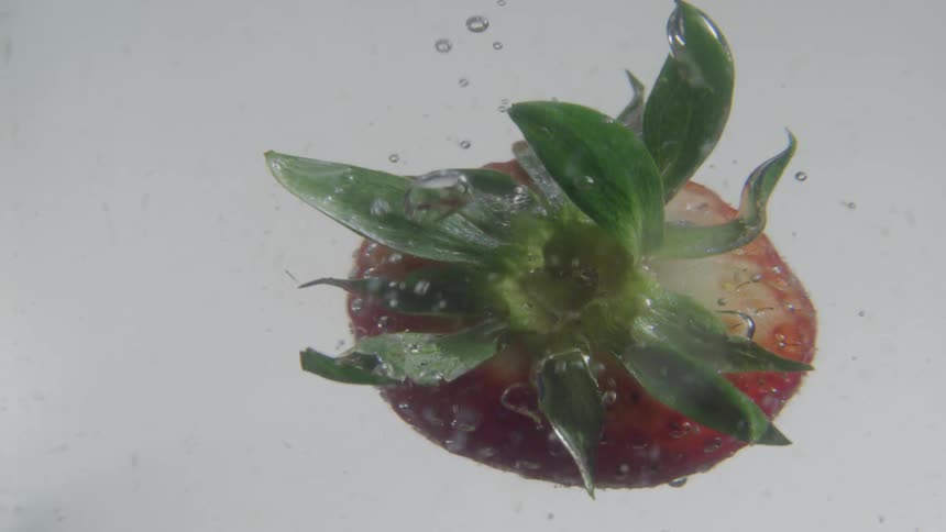 A strawberry falling in a clear liquid before towards the top