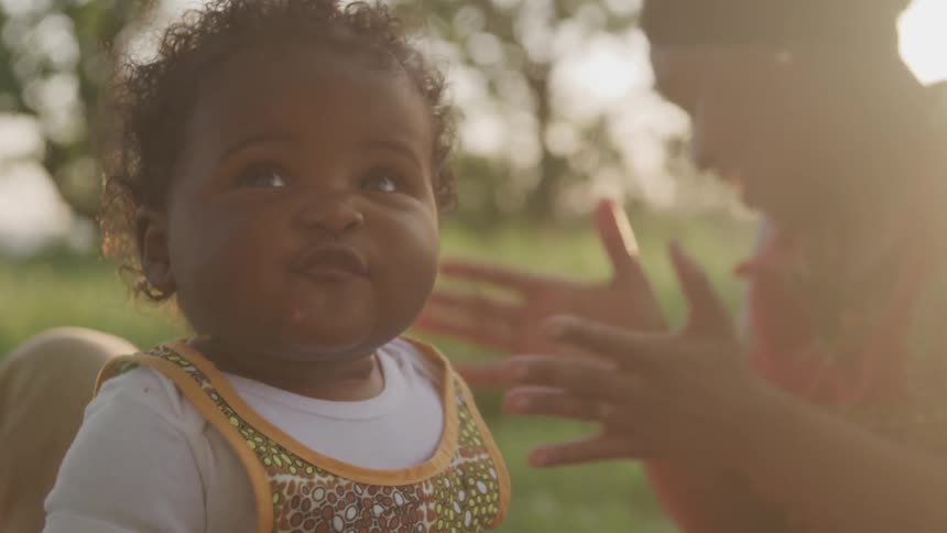 A mother claps for her smiling baby as they play in the park