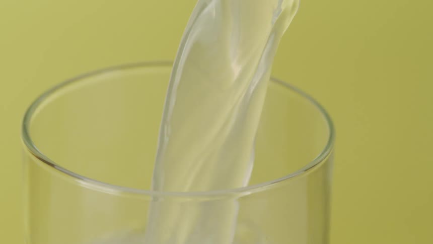 A glass is filled up with a translucent liquid against a yellow background