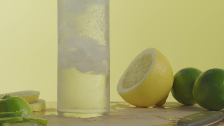 Ice rises in a clear glass sitting next to lemons and limes
