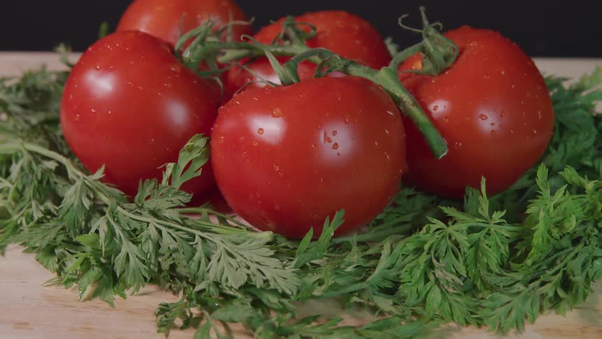 Wet red tomatoes sit on a bed of herbs on a cutting board