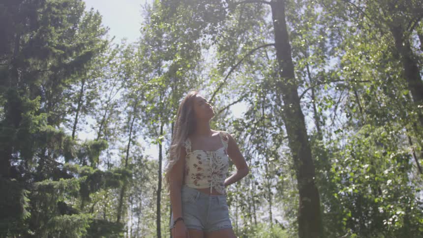 A woman is standing outdoors in a wooded area