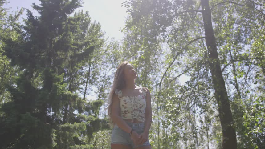 A woman surrounded by trees stares into the sky