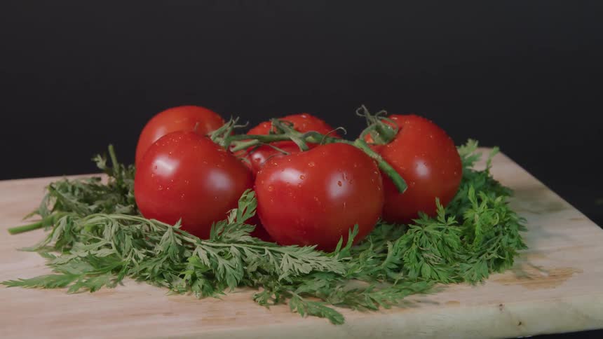 Red ripe vine tomatoes sit on a bed of greens on a cutting board