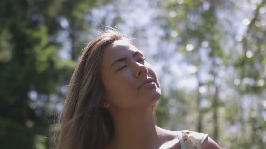A young woman looks up to the sky with her eyes closed