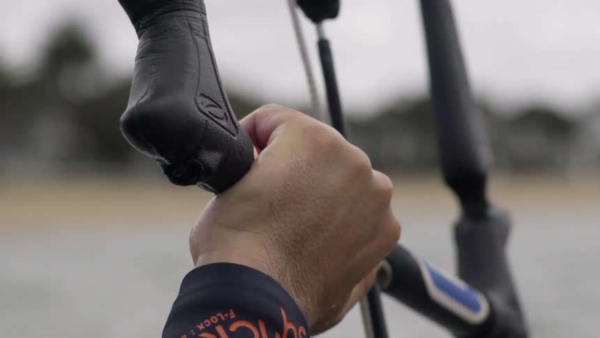 A hand is holding onto a bar by the water on a cloudy day