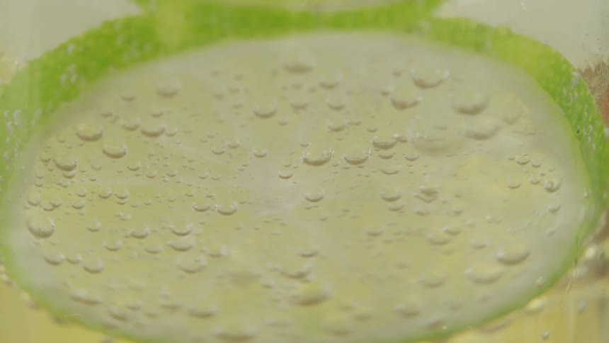 Bubbles in a drink cling to then rise up past a lime slice and ice cubes